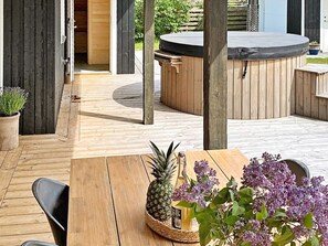 Eine Holzdielen-Terrasse mit Whirlpool, einem Tisch mit Ananas und Blumen sowie Stühlen.