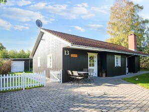 A wooden building with a number 13 sign, a white picket fence, and a paved patio area with outdoor furniture.