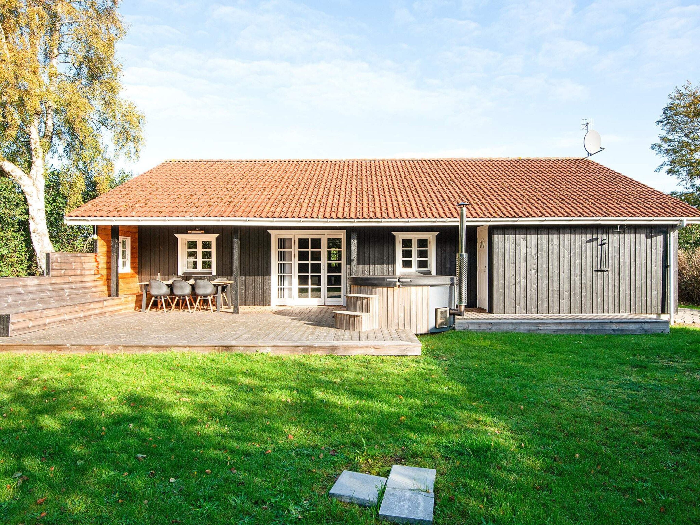 A house with a tiled roof, a deck with outdoor furniture, and a fenced yard.