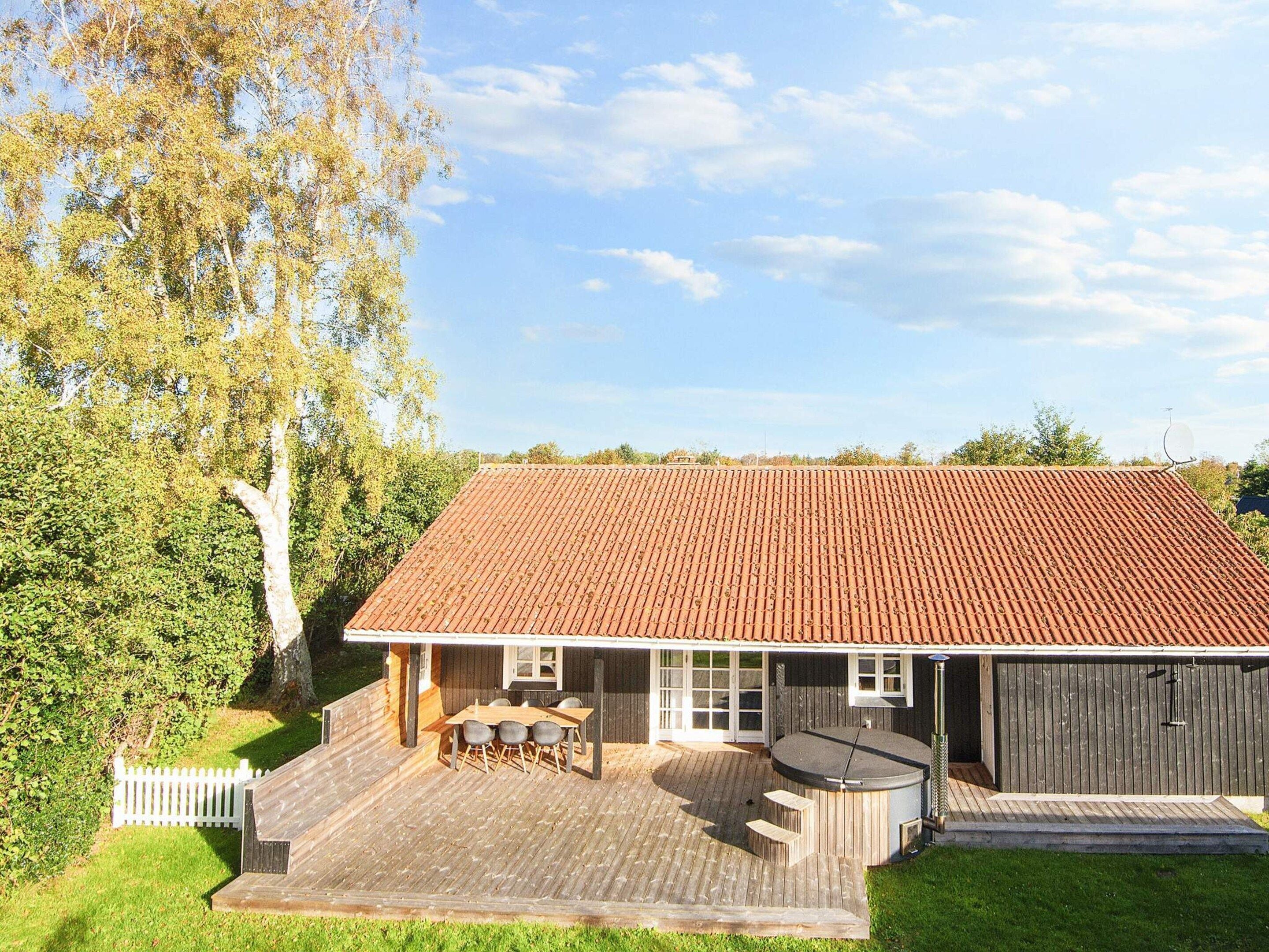 A house with a red-tiled roof, a wooden deck, and a hot tub.