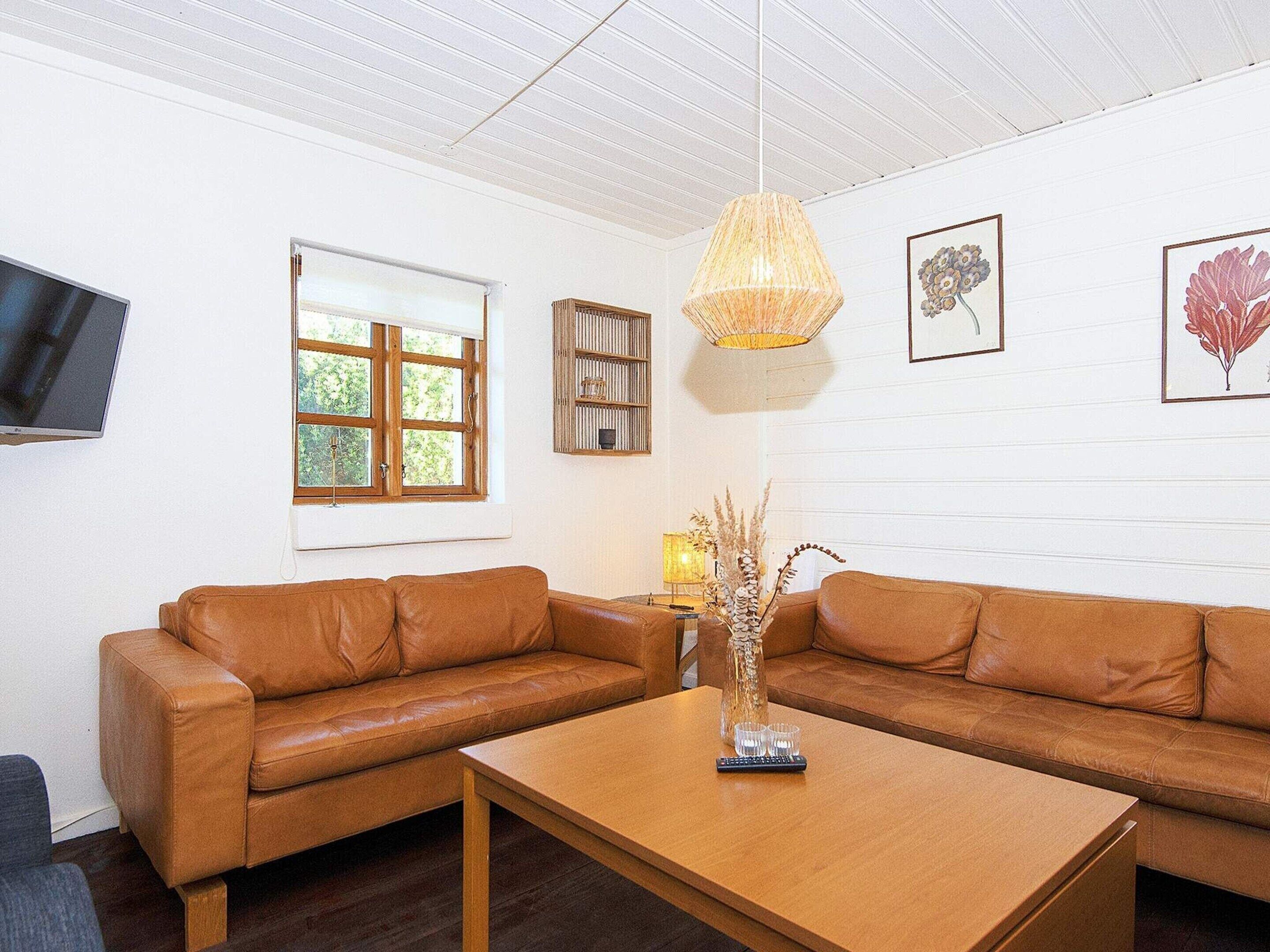 A modern living room with a brown leather sofa, a wooden coffee table, and a hanging woven light fixture.