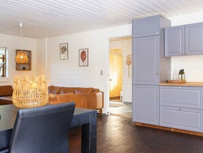 A modern interior with a dining area, a sofa, a kitchen with grey cabinets, and a hanging light fixture.
