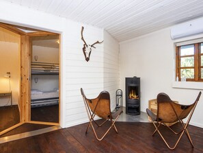 A cozy room with a fireplace, two leather chairs, a bed with a wooden headboard, and a wall-mounted deer skull decoration.