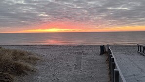Une plage avec une promenade en bois menant à l’eau, un ciel nuageux et un coucher de soleil.