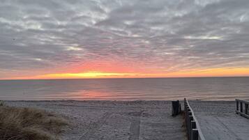 A beach with a wooden walkway leading to the water, a cloudy sky, and a sunset.