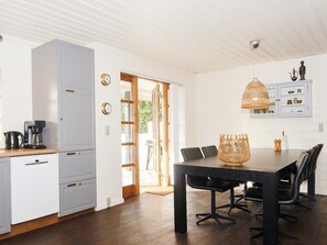 A modern kitchen with a dining area, wooden cabinets, a coffee maker, and a wicker chandelier.