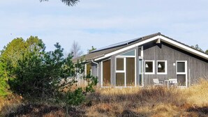 En modern stuga med ett sluttande tak, stora fönster och en uteplats med utemöbler.