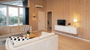 Ett modernt vardagsrum med väggar beklädda med träpaneler, en platt-TV, en soffa, ett soffbord och en lampa.
