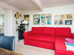A living room with a red sofa, a small table with a lamp, and a wall adorned with framed pictures.