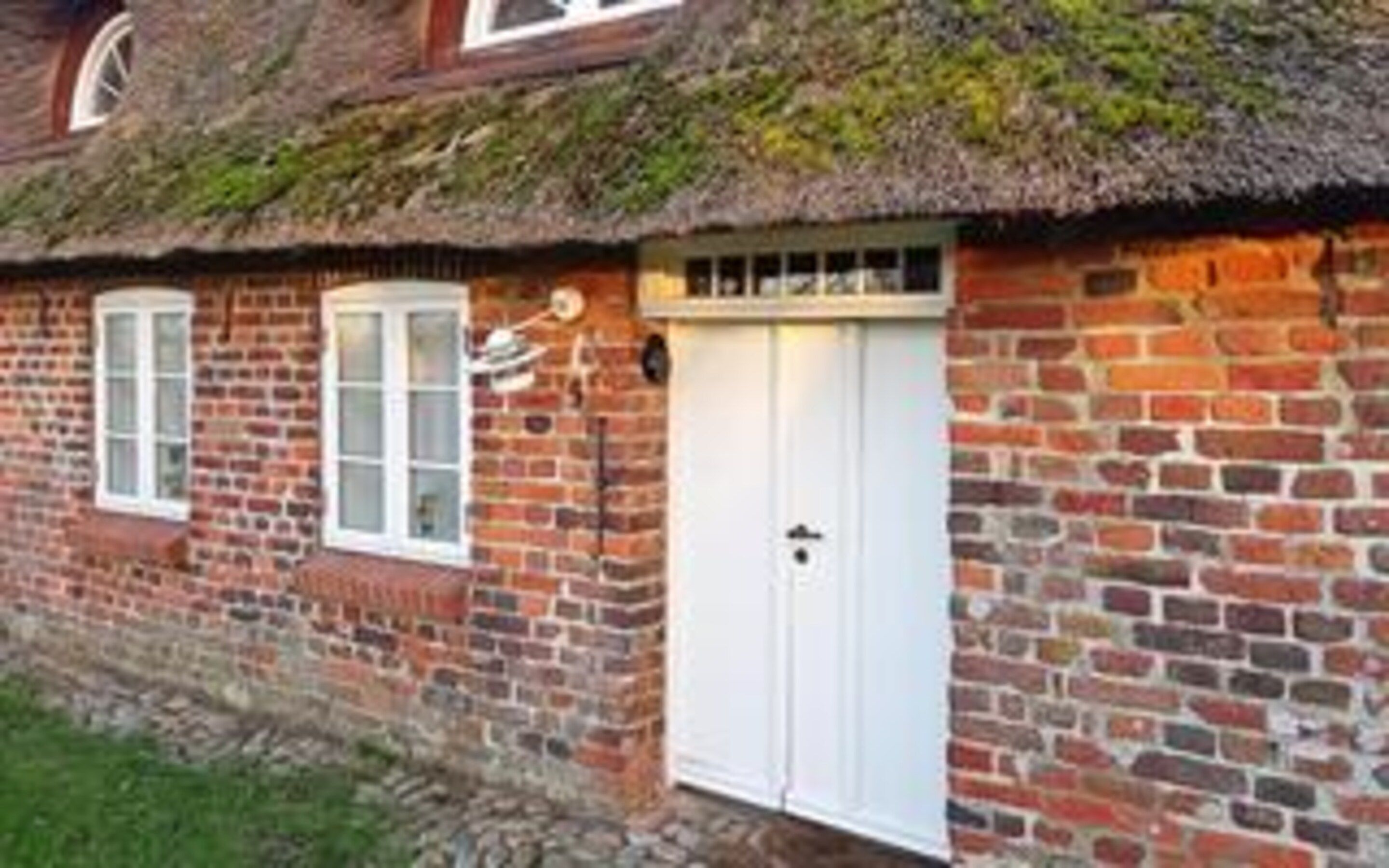 Una casa de ladrillo con tejado de paja, puertas y ventanas blancas.