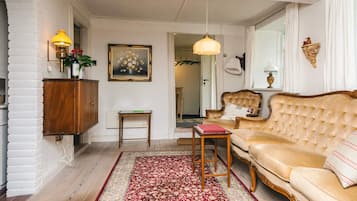 A living room with a sofa, a small table, a rug, a cabinet, a painting, and a hanging light fixture.
