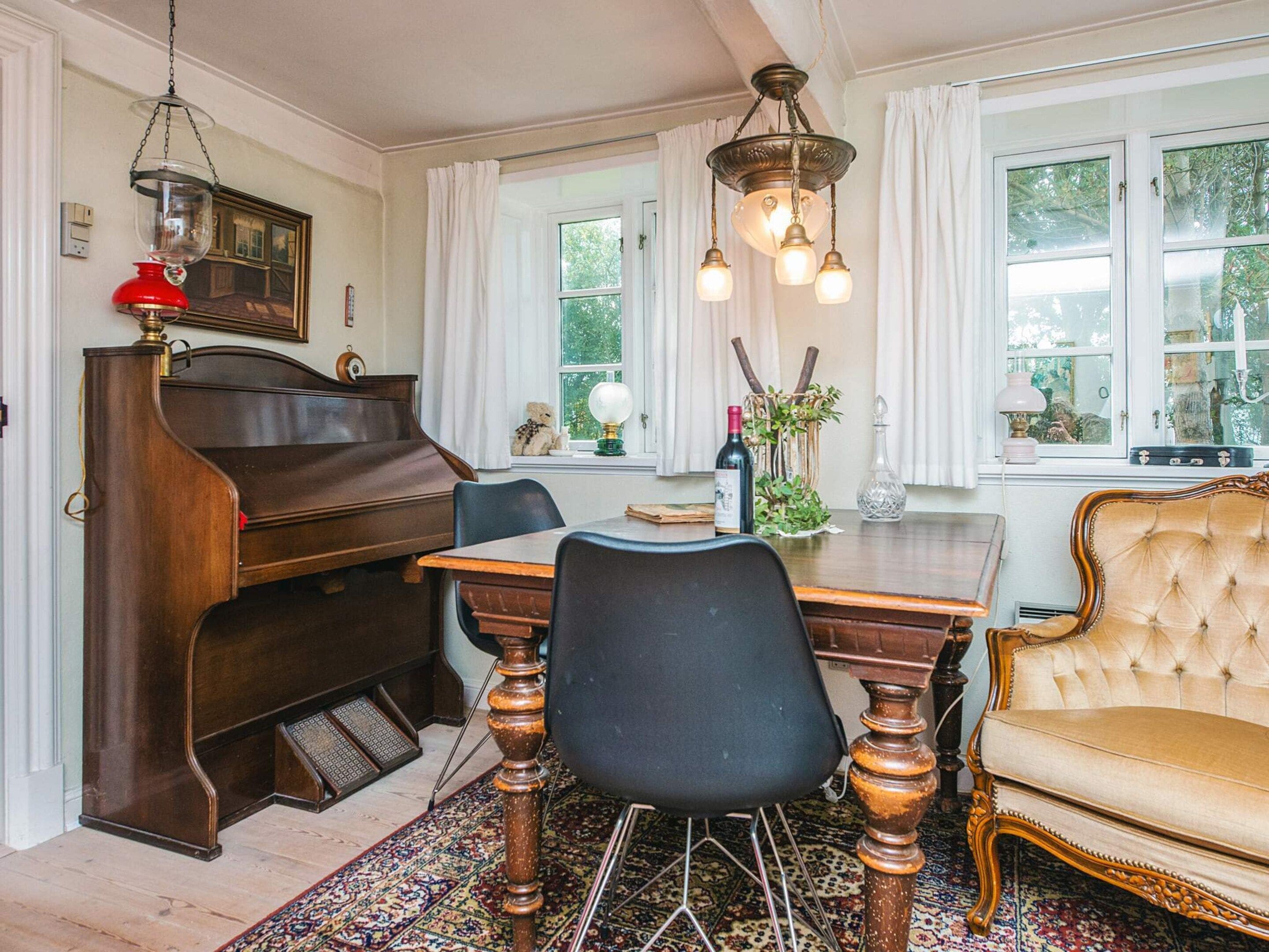A dining area with a wooden table, chairs, a piano, and a chandelier.
