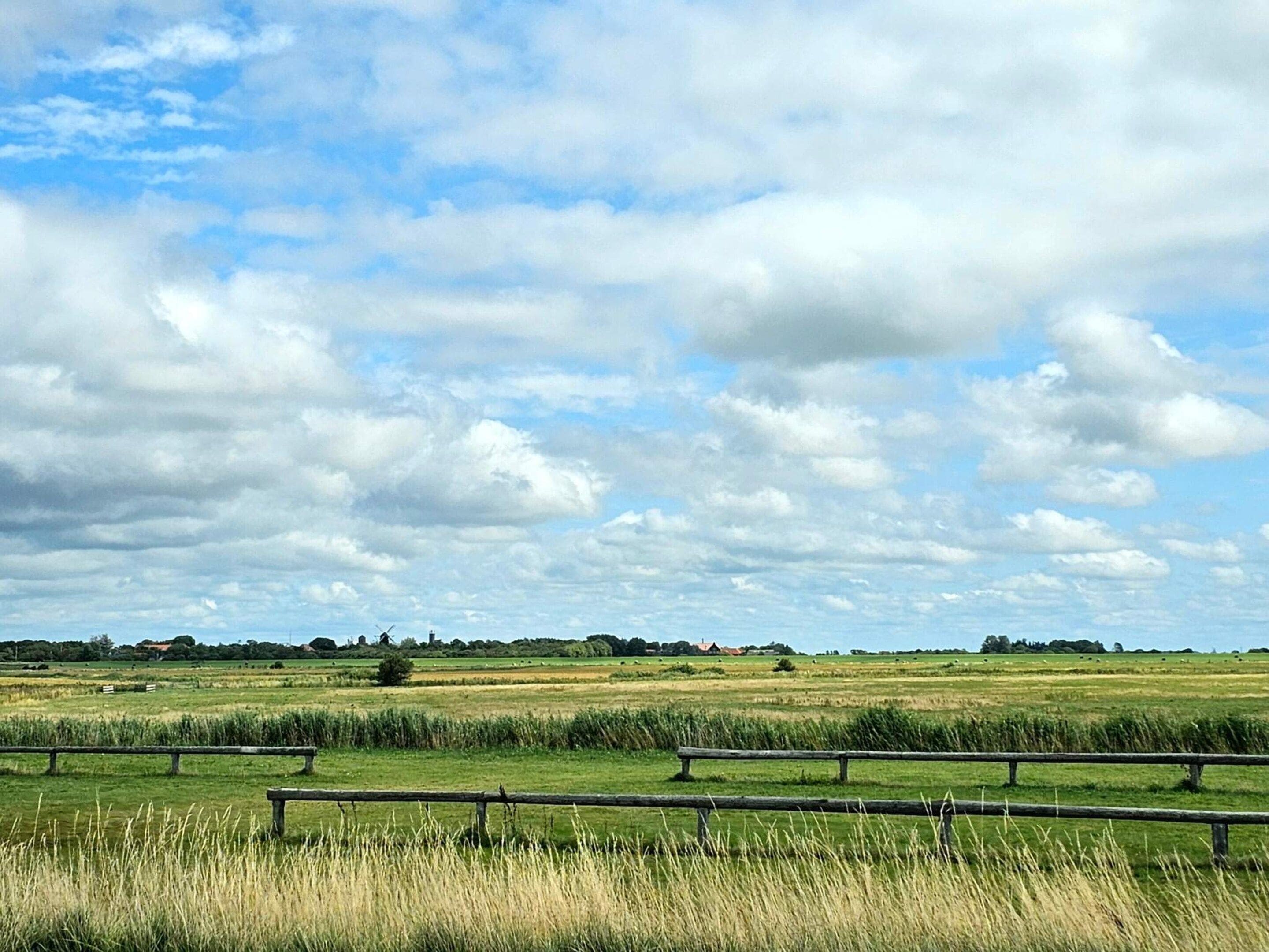 A rural landscape with fields, a wooden fence, and a partly cloudy sky.