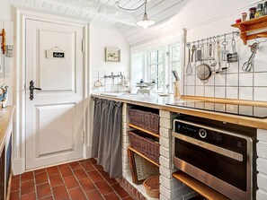 Une cuisine avec une porte blanche, un porte-ustensiles suspendu, un four encastré et un pare-feu en carreaux.