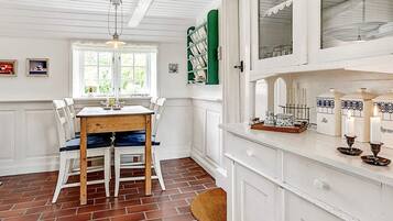 A dining area with a wooden table and white chairs, a window with curtains, and a white cabinet with decorative items.