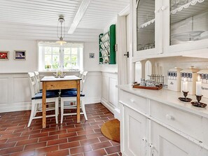 A dining area with a wooden table and white chairs, a window with curtains, and a white cabinet with decorative items.