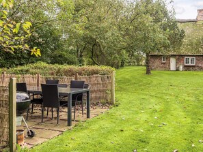 A patio with a table and chairs, a grill, and a thatched-roof building in the background.