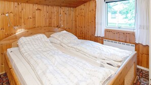 A wooden-paneled room with a bed, a window with curtains, and a wall-mounted heater. - 6 Person Holiday Home in Dannemare (Dannemare)