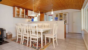 A dining area with a wooden ceiling, white chairs, a central table, and a patterned rug. - 6 Person Holiday Home in Dannemare (Dannemare)
