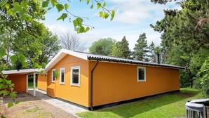 A single-story wooden cabin with a sloped roof, a covered porch, and a small attached structure. - 6 Person Holiday Home in Dannemare (Dannemare)