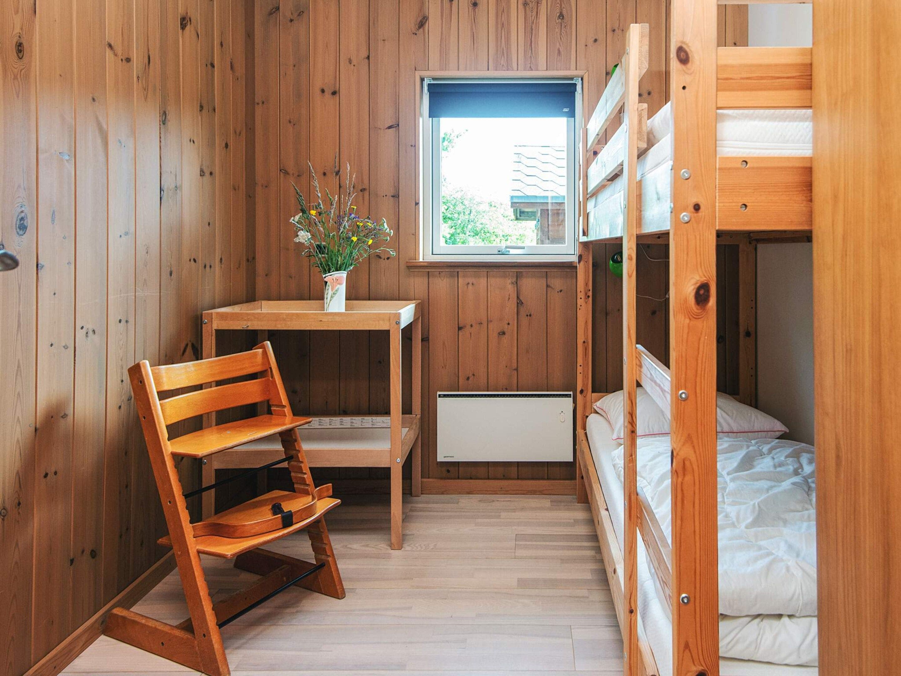 A compact room with wooden walls, a bunk bed, a desk with a chair, and a window.