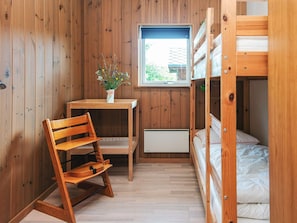 A compact room with wooden walls, a bunk bed, a desk with a chair, and a window.