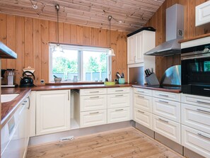 A kitchen with wooden walls, white cabinets, a window, and modern appliances. - Holiday Home in Glesborg (Glesborg)