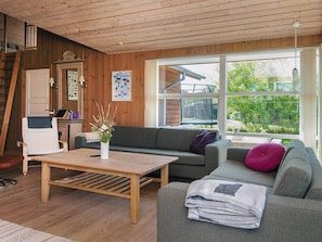 A cozy living room with a wooden ceiling, a sofa, a coffee table, and a window with a view of greenery.