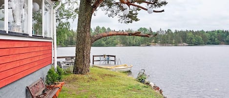 A lakeside property with a red building, a dock, a boat, and a tree.