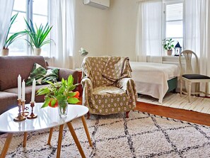 A cozy living room with a sofa, a patterned armchair, a small table with candles, and a vase with flowers. - 5 Person Holiday Home in Akersberga (Akersberga)