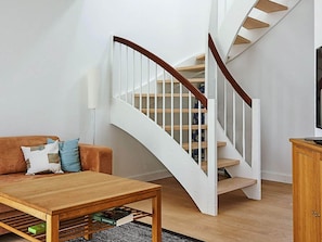 A living room with a wooden coffee table, a brown sofa with cushions, a white staircase with wooden steps, and a television on a wooden cabinet.