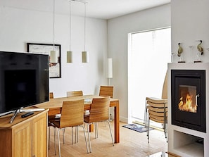 A modern living room with a TV, dining table, chairs, a fireplace, and pendant lights.