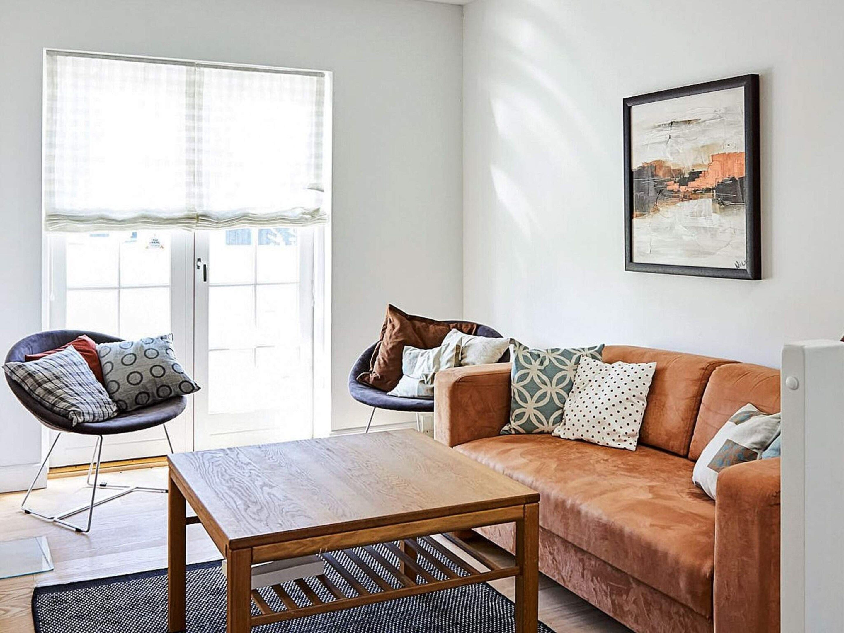 A living room with a wooden coffee table, a brown sofa, and two armchairs with cushions.