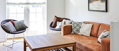 A living room with a wooden coffee table, a brown sofa, and two armchairs with cushions.