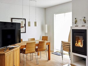 A modern living room with a flat-screen TV, wooden dining table, chairs, a fireplace, and pendant lights.