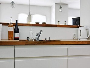 A modern kitchen with a wooden countertop, a sink, a kettle, and a wine bottle. - Holiday Home in NykÃ¸bing Sj (Nykobing Sjaelland)