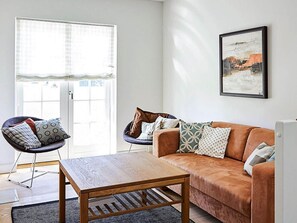 A living room with a sofa, a chair, a coffee table, a door with a view, and a framed picture on the wall.