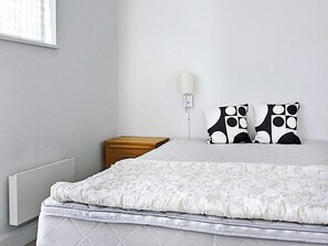 A bedroom with a bed, a bedside table, a wall-mounted lamp, and a radiator. - Holiday Home in NykÃ¸bing Sj (Nykobing Sjaelland)