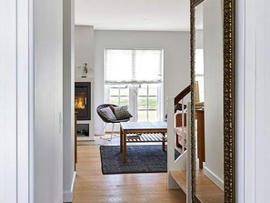 A hallway leading to a living room with a fireplace, a chair, a table, and a large mirror.
