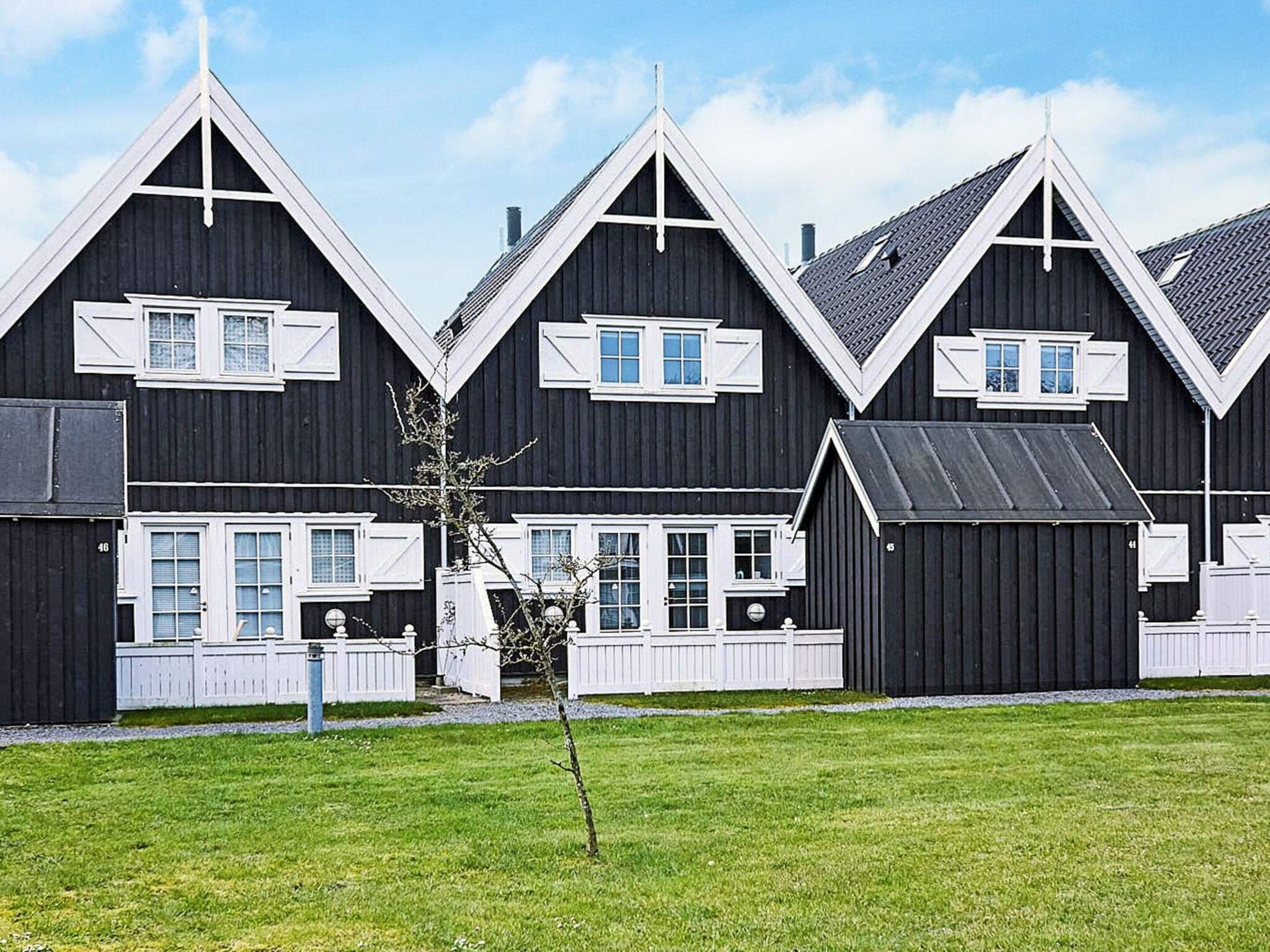 Una hilera de casas de madera oscura con detalles blancos y numerosas ventanas, cada una con contraventanas.