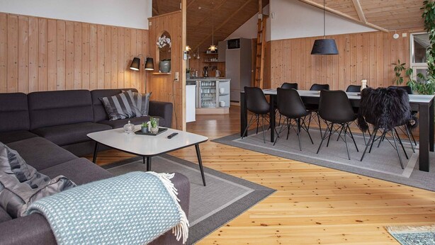 Ett rymligt vardagsrum med ett träpanelat tak, en soffa, ett soffbord och en matplats med stolar och ett bord.