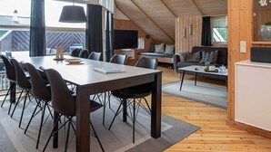 Ett modernt rum i loftstil med högt i tak, en matplats med ett långt bord och stolar, en mysig sittgrupp med en soffa och ett soffbord samt ett köksområde med ett inbyggt skåp.