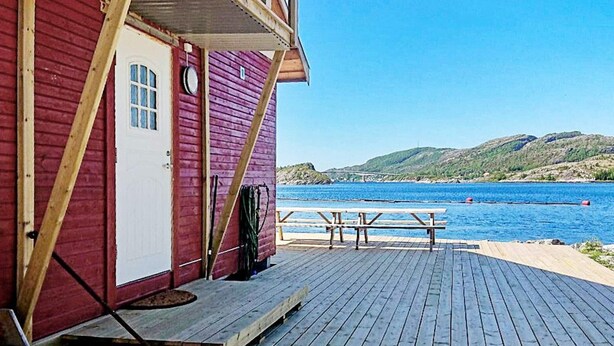 A wooden deck with a picnic table and benches, leading to a building with a red exterior and a white door. - 8 Person Holiday Home in Revsnes (Åfjord)