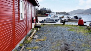 A red building with a dock extending into a calm body of water, surrounded by boats and a distant house. - 8 Person Holiday Home in Revsnes (Åfjord)