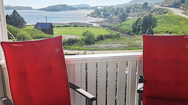 Two red chairs on a wooden deck with a view of a coastal landscape. - 8 Person Holiday Home in Revsnes (Åfjord)