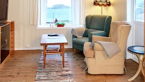 A cozy room with a view of the sea, a green armchair, a beige armchair, a small table with a remote control, and a lamp. - 8 Person Holiday Home in Revsnes (Åfjord)