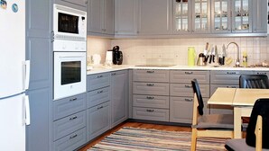 A kitchen with grey cabinets, a white refrigerator, a microwave, and a coffee maker. There is a striped rug on the floor and a table with chairs. - 8 Person Holiday Home in Revsnes (Åfjord)