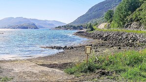 A coastal road with a rocky shoreline, a small building, and mountains in the background. - 8 Person Holiday Home in Revsnes (Åfjord)