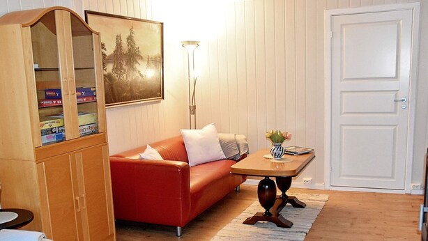 A living room with a red sofa, a wooden cabinet with books, a table with a vase, and a door. - 8 Person Holiday Home in Revsnes (Åfjord)