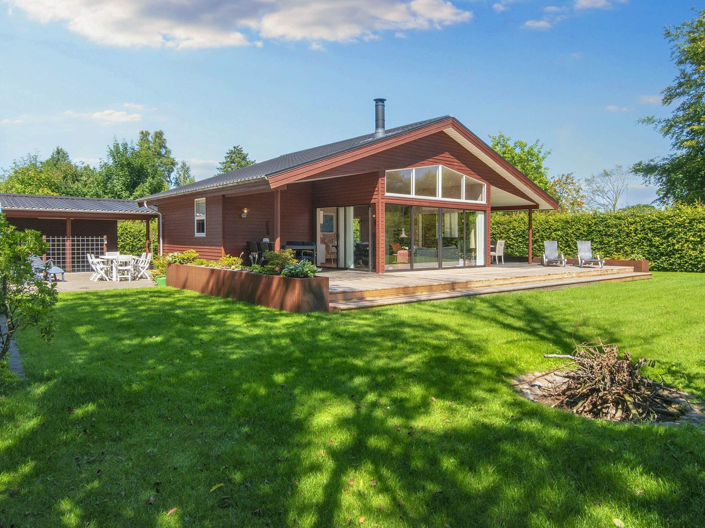 Une maison moderne dotée d’un patio couvert, d’une pelouse et d’un foyer extérieur.
